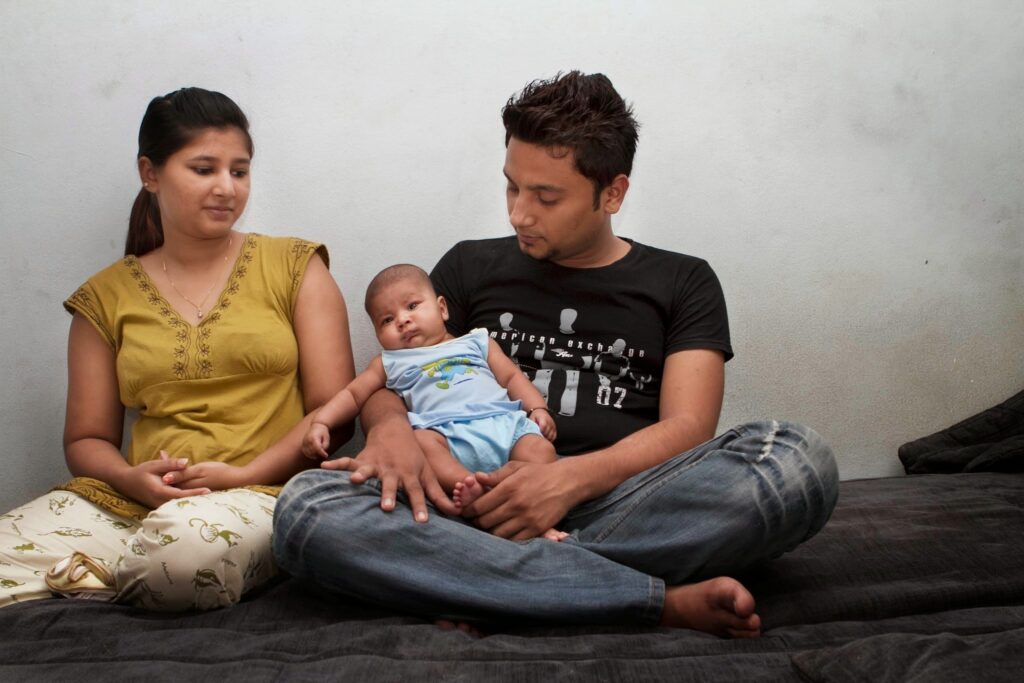 Image shows a couple sitting on a bed holding their baby.