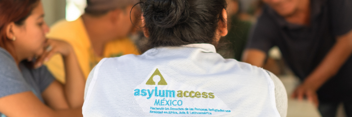 Image shows a member of Asylum Access Mexico staff from behind wearing a white shirt with the organization logo